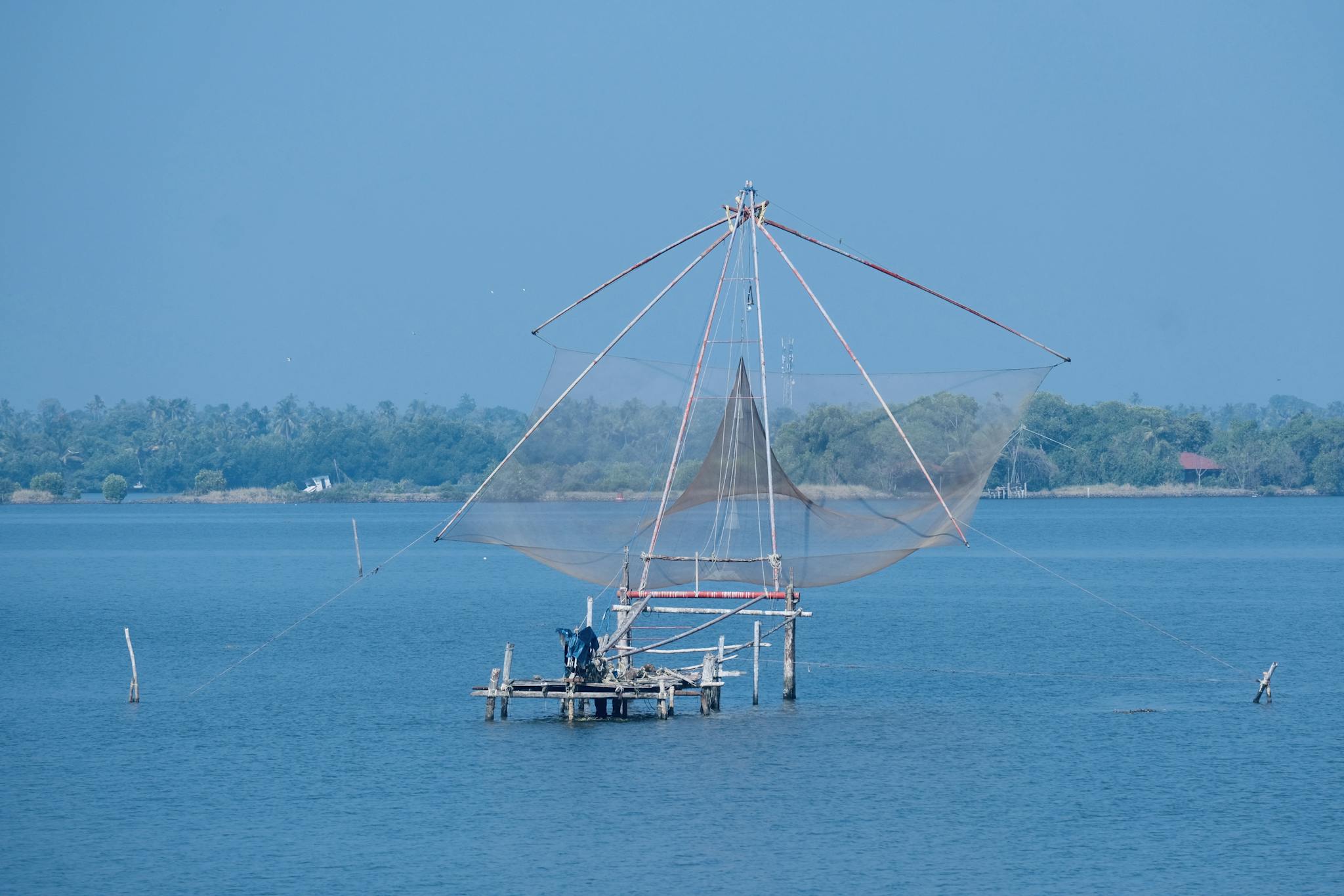A picturesque view of a large Chinese fishing net on a tranquil coastline under a blue sky.