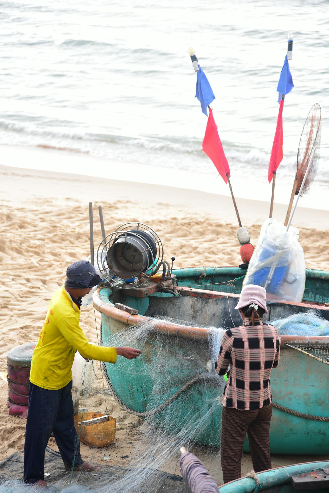Fishermen working with nets on a sandy beach near the ocean.